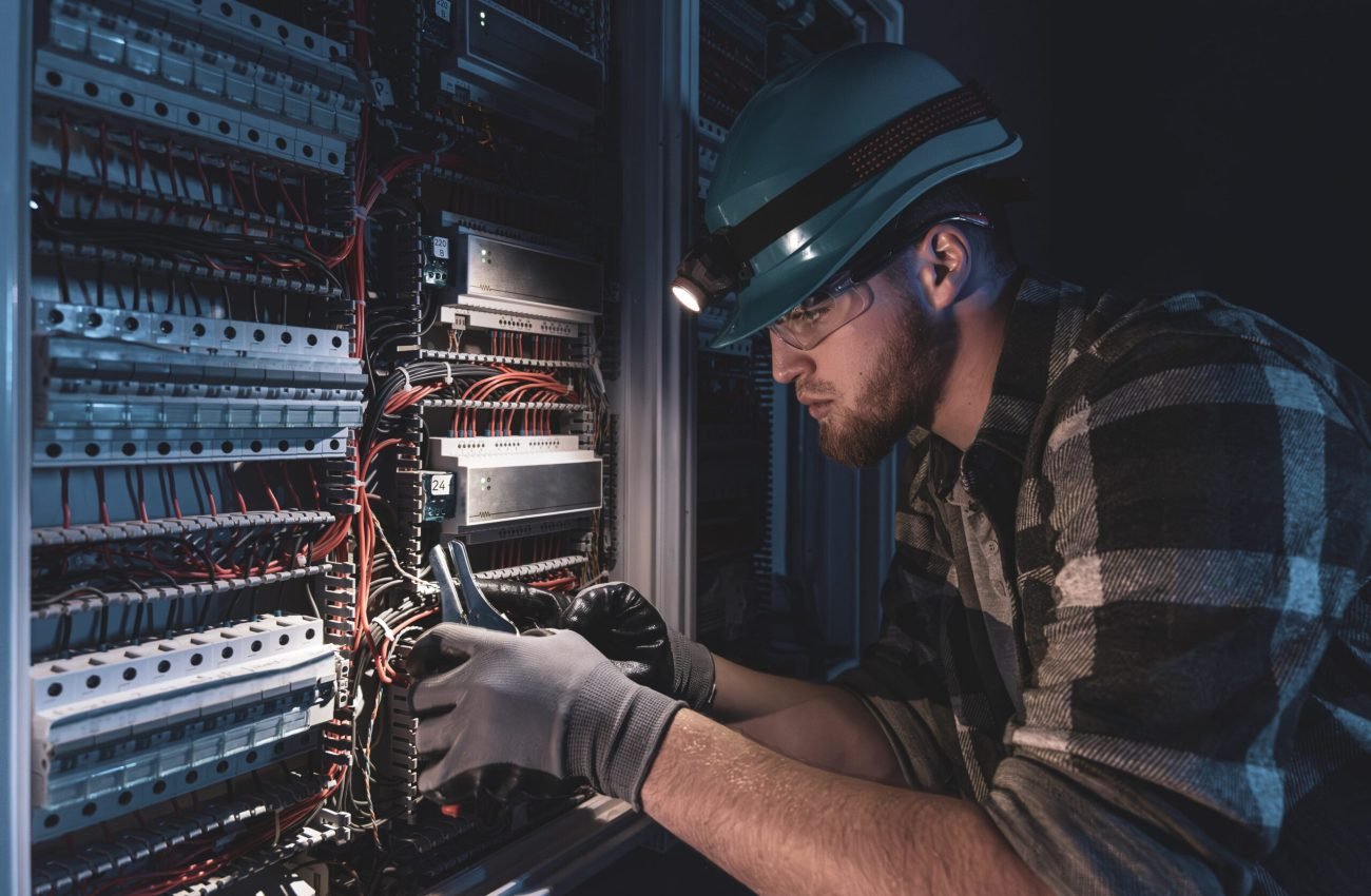 male-electrician-works-switchboard-overalls-against-backdrop-emergency-lighting (1) (1)